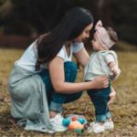 A young mother crouching down to hold her baby girl toodler