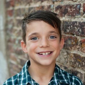 A photo of a young boy with brown hair and a plaid shirt smiling 