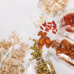 A tabletop view of an array of glass jars with nuts spilled on a white table